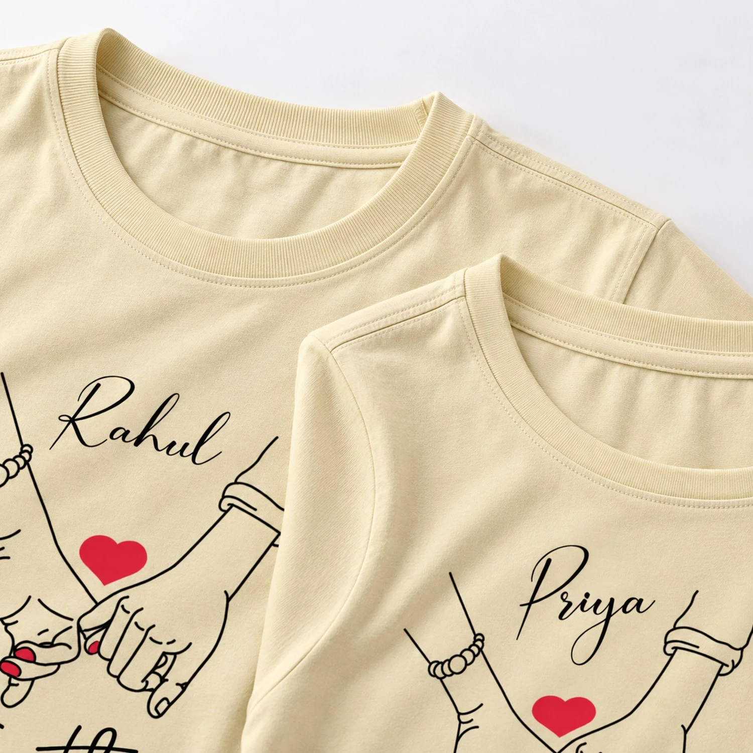 Close-up of two pale yellow personalized couple T-shirts showing the necklines and Rahul and Priya custom name prints with romantic hand artwork.