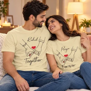 Couple cuddling on a sofa in personalized pale yellow Rahul and Priya T-shirts with red hearts, hand line art, and Together Forever lettering.