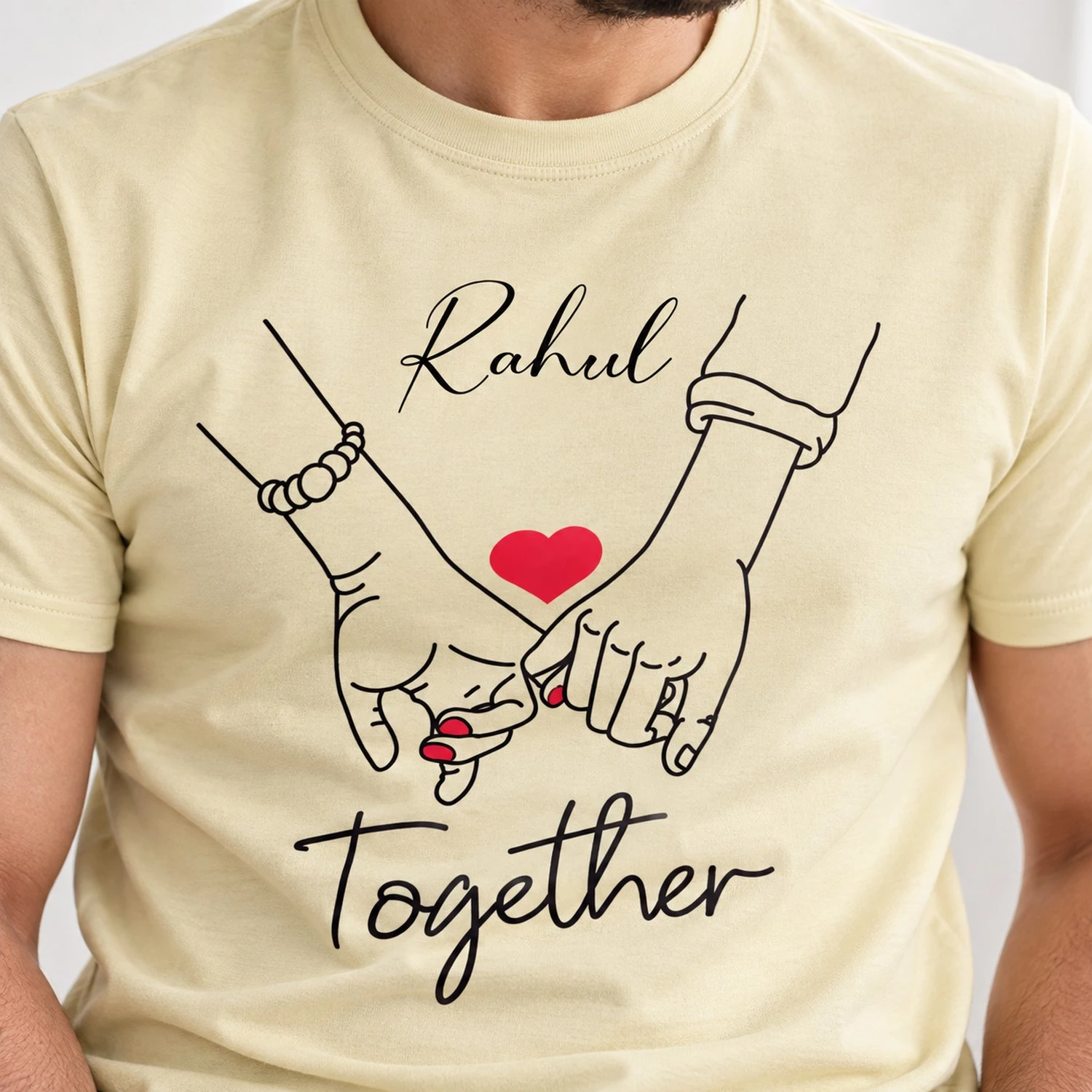 Close-up of a pale yellow personalized men’s couple T-shirt printed with Rahul, holding-hands line art, a red heart, and Together text.