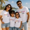 Family of four wearing matching white Vacay Mode T-shirts for parents and kids on a tropical beach