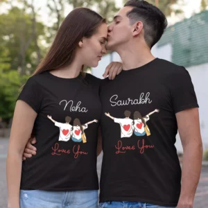 A couple wearing black t-shirts. The woman's shirt has a cartoon drawing of a couple with her name "Neha" and the text "Loves You." The man's shirt has a similar drawing with his name "Saurabh" and the text "Loves You." He is kissing her on the forehead.
