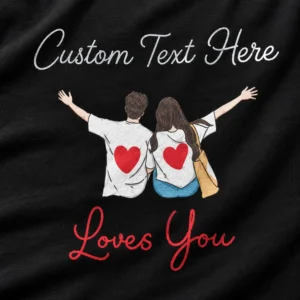 Close-up of a black personalised couple T-shirt showing custom text, cartoon couple artwork with red hearts, and red Loves You script.