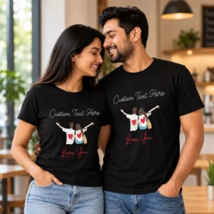 Couple standing together indoors wearing matching black personalised T-shirts with custom text, cartoon couple illustration, red hearts, and Loves You lettering.