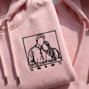 Close-up view of custom line-art portrait embroidery on pink couple hoodies.