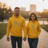 A smiling couple, Nakul and Tanya, holding hands and walking in a park at sunset while wearing their personalized yellow matching couple hoodie set.