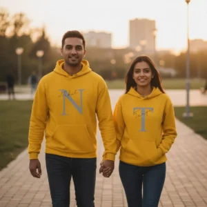 A smiling couple, Nakul and Tanya, holding hands and walking in a park at sunset while wearing their personalized yellow matching couple hoodie set.