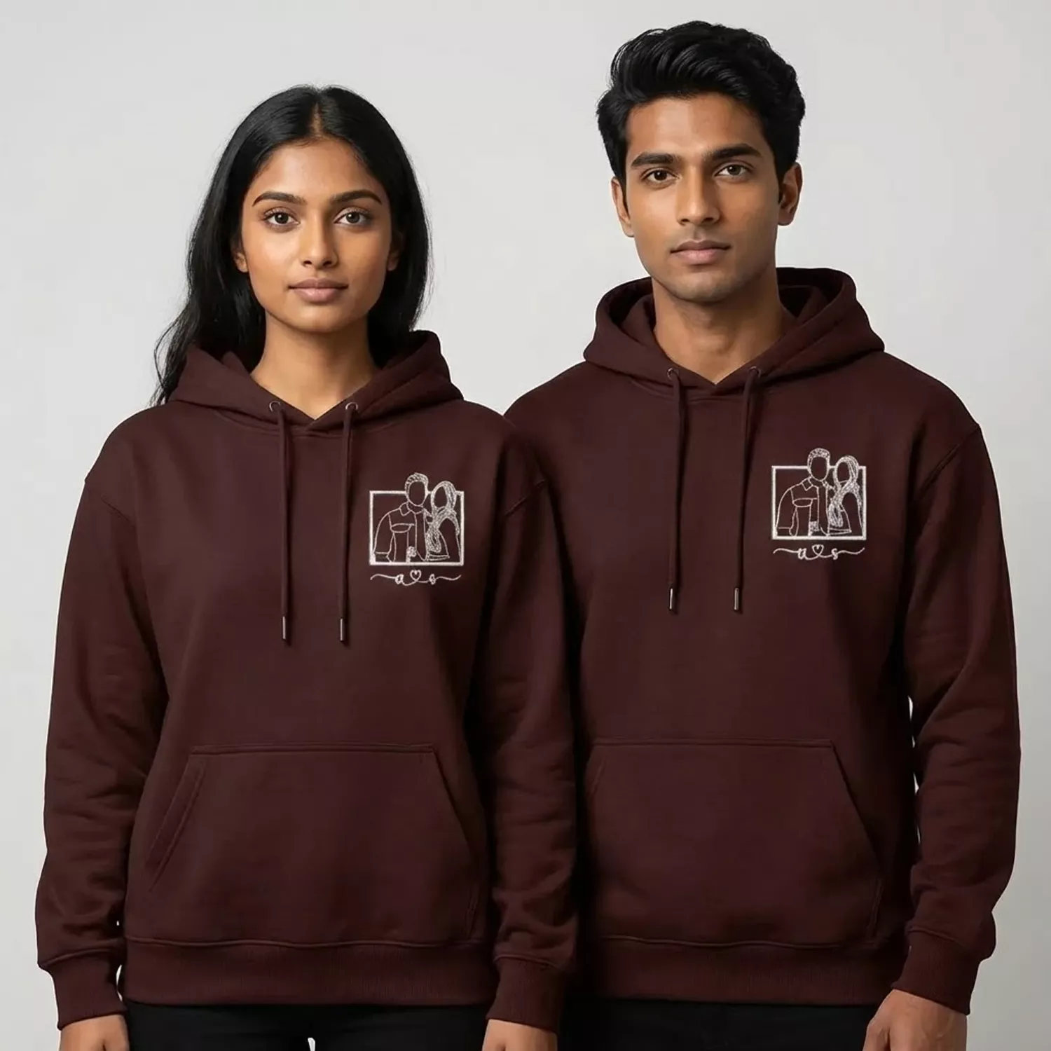 Couple wearing maroon custom embroidered hoodies with white line-art portrait design