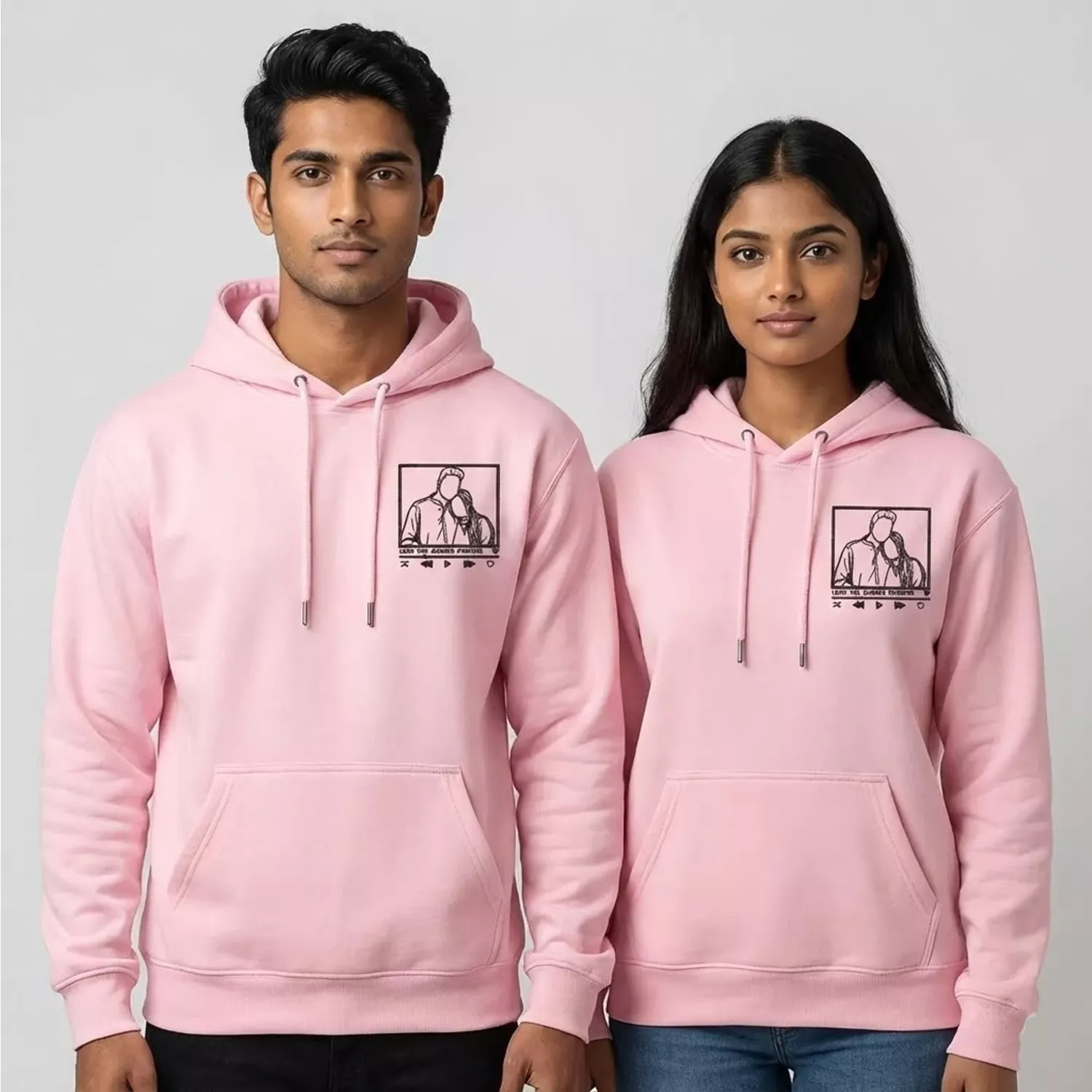 Man and woman wearing matching pink hoodies with custom line-art portrait embroidery.