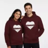 Matching custom name couple hoodies in maroon with heart design worn by a smiling couple.