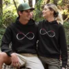Matching black custom name split design couple hoodies with infinity heart print for couples sitting outdoors