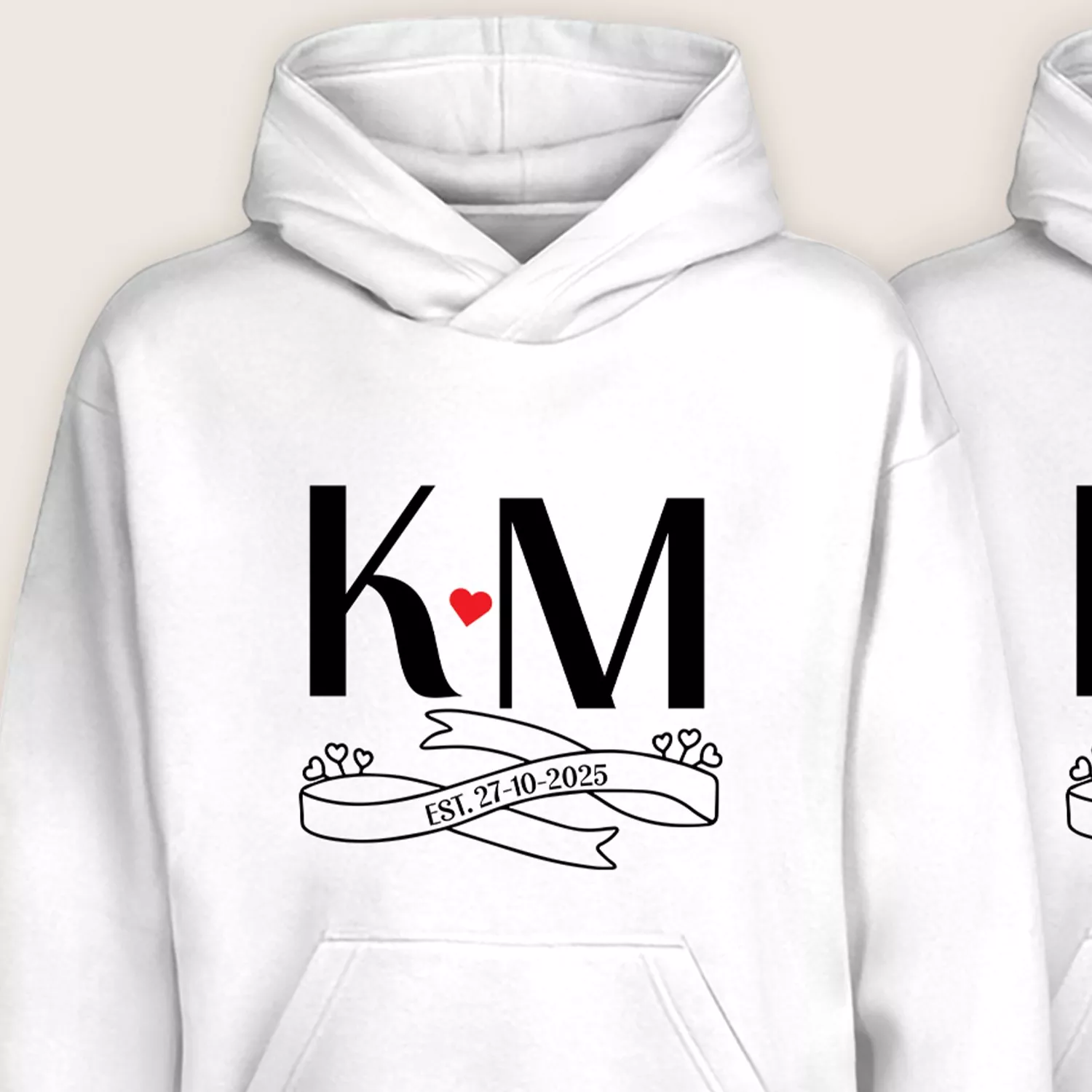 Close-up view of personalized KM initials couple hoodie with heart and EST. 27-10-2025 printed on white fabric.