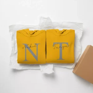 The 'Nakul' and 'Tanya' matching couple hoodie set, neatly folded on white tissue paper, shown next to a shipping box.