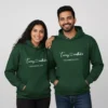 A couple wearing matching green custom matching couple name hoodies and date printed on the front.
