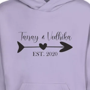 Close-up of minimal name printed couple hoodie with custom names and arrow heart design in black on lavender fabric – personalized matching hoodie for couples.