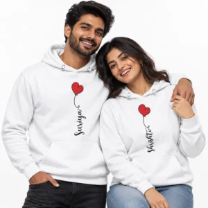 Smiling couple wearing matching white personalized couple hoodies with custom vertical name prints and red heart balloon designs.