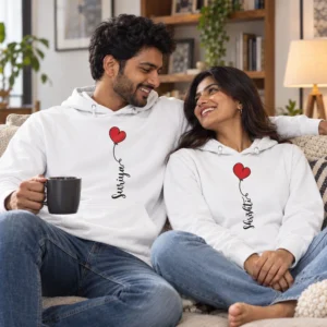 Couple relaxing together on a sofa wearing matching white personalized hoodies with custom names and red heart designs.