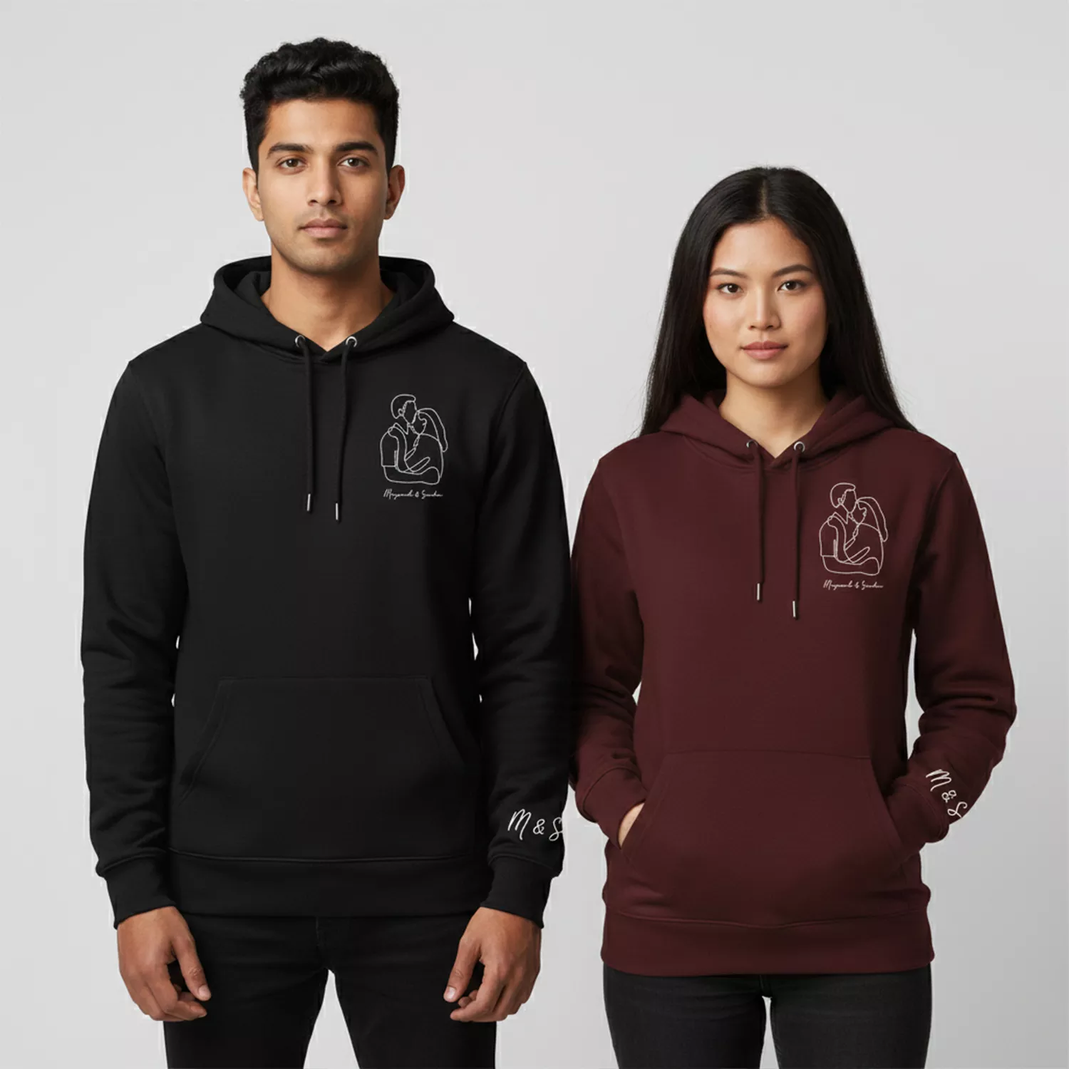 Couple wearing personalized hoodies in black and maroon with line-art design, custom names, and sleeve initials