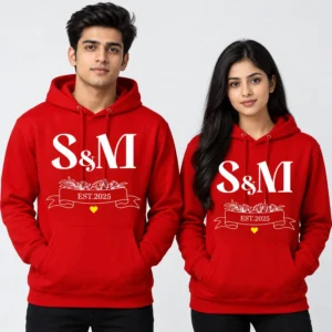 Red personalized couple hoodies with white S and M initials, floral ribbon, EST. 2025 text, and a small yellow heart.