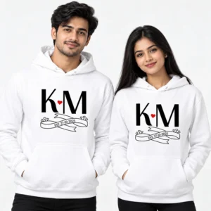 White personalized initial couple hoodies with K and M monogram, red heart, ribbon detail, and EST. 27-10-2025 date.