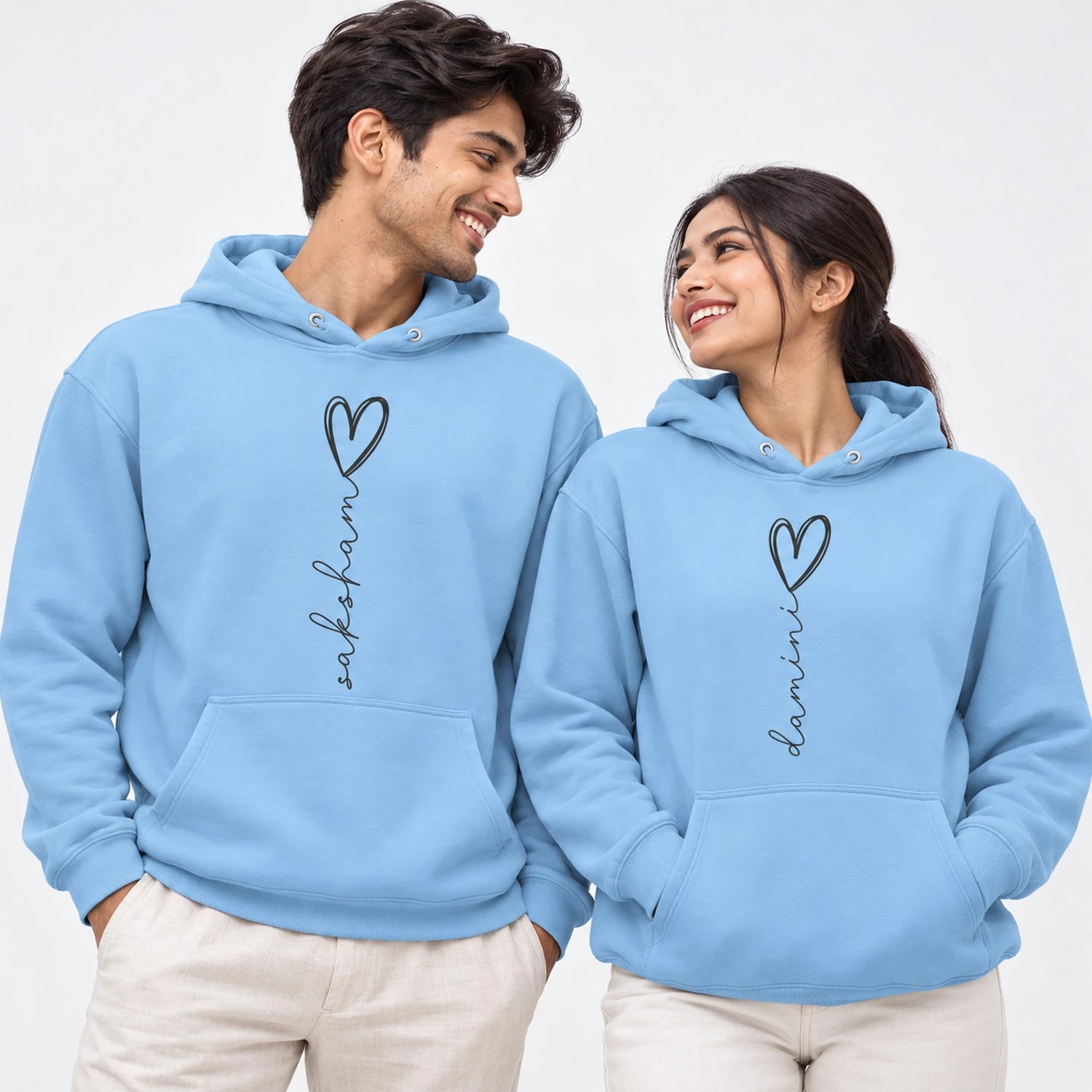 Light blue personalized name couple hoodies with vertical black script names ending in outlined heart designs.