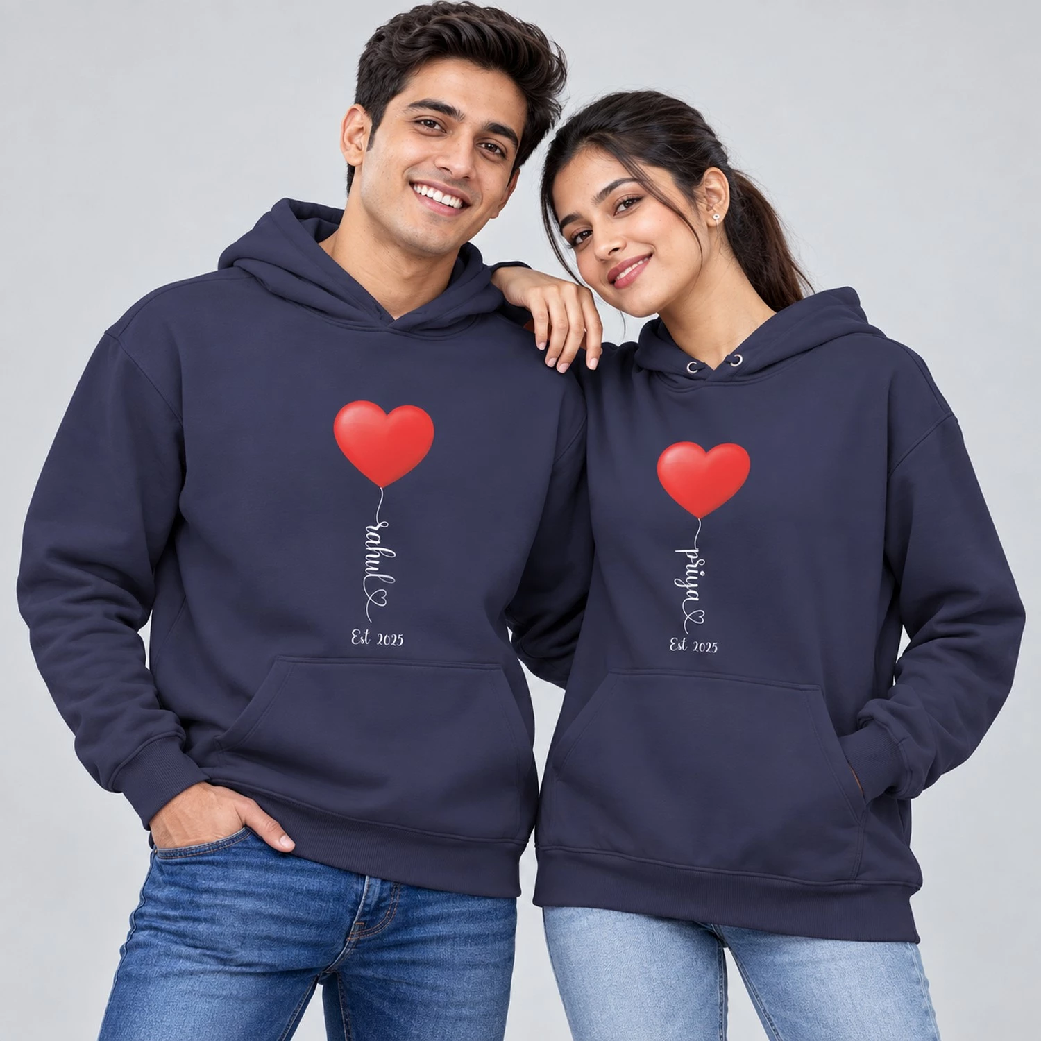 Personalized name printed couple hoodies in navy blue with red heart balloon graphics, Rahul and Priya names, and Est 2025 text.