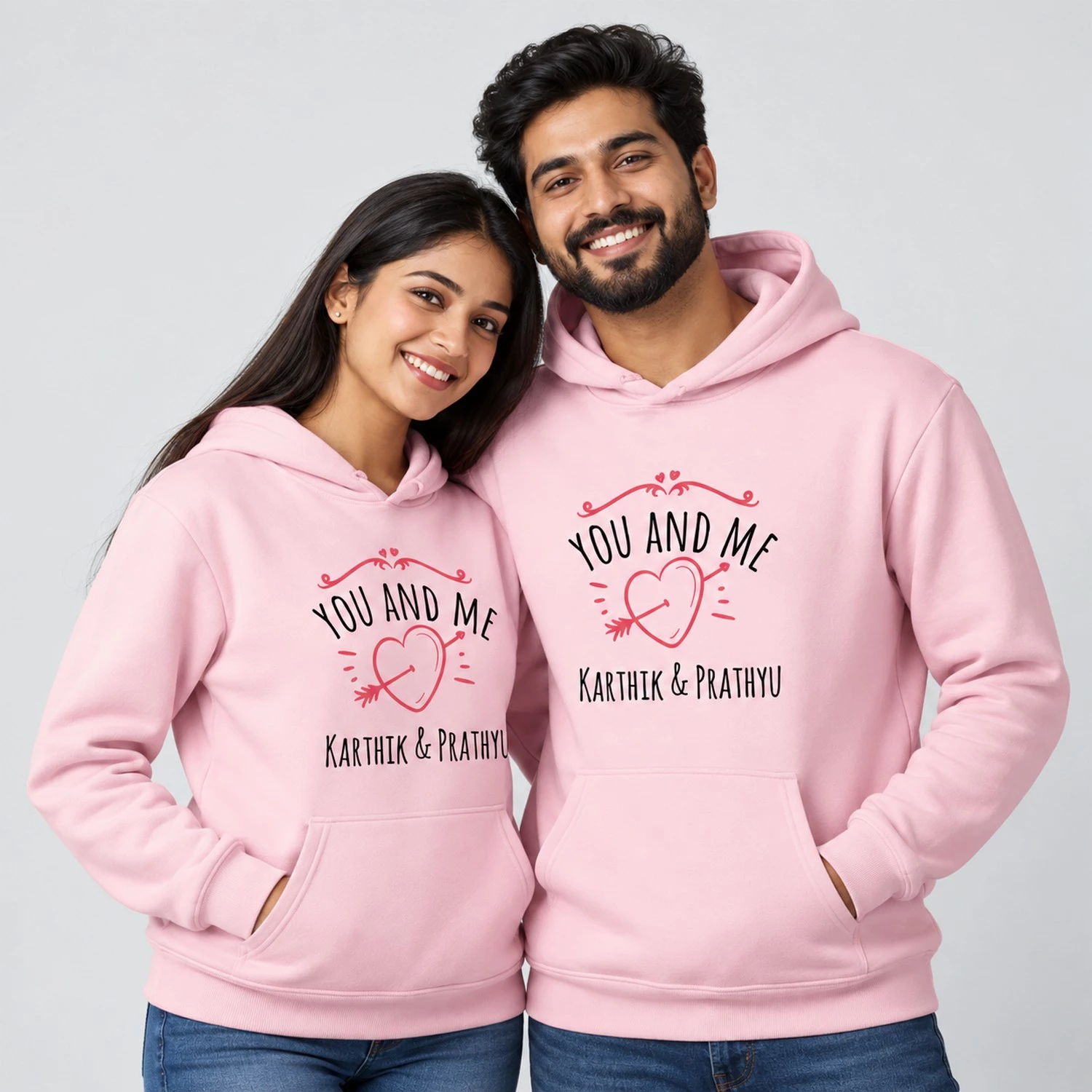 Pink personalized name couple hoodies with You and Me text, heart-and-arrow artwork, and Karthik and Prathyu names.