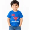 Smiling little boy wearing a royal blue personalized kids T-shirt featuring a playful red and pink cartoon dinosaur with the words DHRUV SAURUS in white distressed lettering.