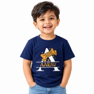 Smiling toddler boy wearing a navy blue personalized T-shirt with a large white letter A, golden yellow bow, small hearts and the name AARAV printed in yellow.