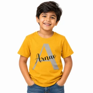 Smiling young boy wearing a mustard yellow personalized T-shirt with a large gray letter A and the name Arnav printed across it in black cursive lettering.