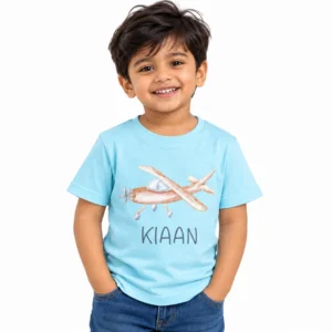 Smiling little boy wearing a sky blue personalized kids T-shirt featuring a watercolor-style airplane illustration and the custom name Kiaan in dark lettering.