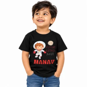 Smiling little boy wearing a black personalized kids T-shirt featuring a cartoon astronaut, moon illustration, Future Astronaut lettering, and the name Manav in bold red text.