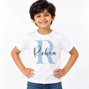 Smiling young boy wearing a white personalized T-shirt featuring a large light blue letter R with the name Rehan overlaid in black handwritten cursive script.