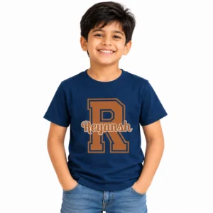 Smiling young boy wearing a navy blue personalized T-shirt featuring a large brown varsity-style letter R with the name Reyansh printed across it in outlined script lettering.