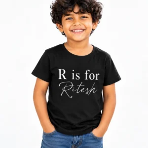 Smiling young boy with curly hair wearing a black personalized kids T-shirt displaying R is for Ritesh in white serif and cursive lettering.