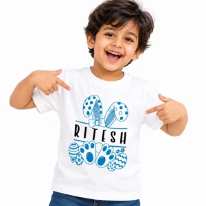 Smiling boy wearing a white personalized kids T-shirt with the name RITESH in black letters, surrounded by blue bunny ears, a bow, paw prints and decorated Easter eggs.