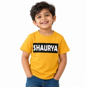 Smiling young boy wearing a yellow personalized kids T-shirt featuring the name SHAURYA in bold white uppercase lettering inside a black rectangular chest print.