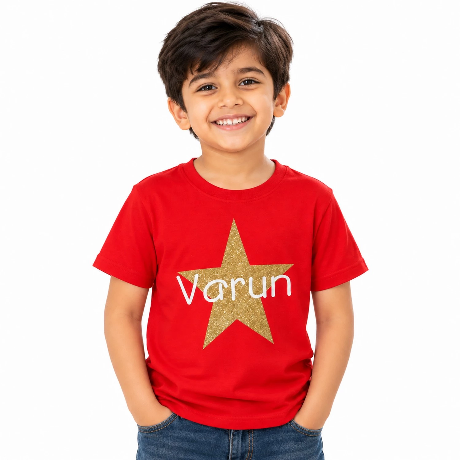 Smiling young boy wearing a red personalized kids T-shirt featuring a large glitter-effect golden star with the name Varun printed across it in white lettering.