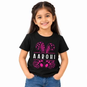 Smiling young girl wearing a black personalized kids T-shirt with the name AAROHI in white letters, surrounded by pink bunny ears, a bow, paw prints and Easter egg illustrations.