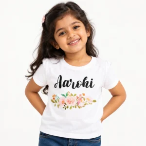 Smiling young girl wearing a white personalized T-shirt featuring the name Aarohi in black cursive lettering above a watercolor floral arrangement of pink and peach flowers.