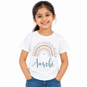 Smiling young girl wearing a white personalized kids T-shirt featuring a pastel rainbow with golden dots, pink and teal arches, a small heart and the name Aarohi in teal cursive lettering.