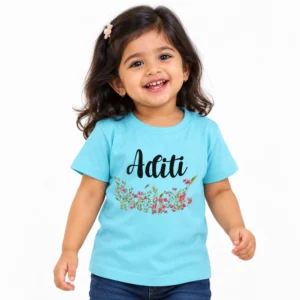 Smiling toddler girl wearing a sky blue personalized kids T-shirt featuring the name Aditi in black script above delicate pink flowers and green leafy stems.