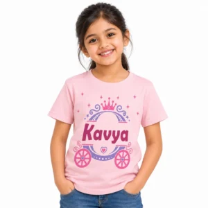 Smiling young girl wearing a light pink personalized T-shirt featuring a princess crown, decorative carriage, hearts, stars, and the name Kavya in bold magenta lettering.