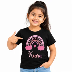 Smiling young girl wearing a black personalized kids T-shirt featuring a pink rainbow with hearts, dotted arches, pink clouds and the name Kiara in cursive lettering.