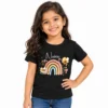Smiling young girl wearing a black personalized T-shirt with the name Naina in white script above a pastel rainbow decorated with cartoon bees, flowers and leaves.