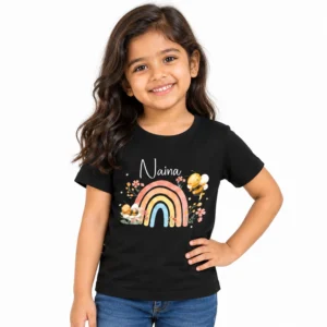 Smiling young girl wearing a black personalized T-shirt with the name Naina in white script above a pastel rainbow decorated with cartoon bees, flowers and leaves.