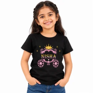 Smiling young girl wearing a black personalized kids T-shirt featuring a pink princess carriage, golden crown, decorative stars and the name NISHA in pink and gold lettering.