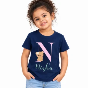 Smiling young girl wearing a navy blue personalized kids T-shirt featuring a large pink N monogram, a cute beige teddy bear with a flower, and the name Nisha in mint green script.