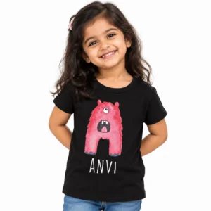 Smiling young girl wearing a black personalized kids T-shirt featuring a pink one-eyed cartoon monster with an open mouth and the name ANVI in white lettering.