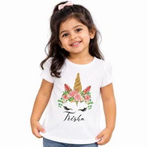 Young girl wearing a white personalized unicorn T-shirt featuring a golden spiral horn, pink floral crown, unicorn eyelashes, and black cursive name Trisha.