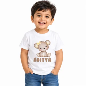 Smiling toddler boy wearing a white personalized kids T-shirt featuring a cute beige teddy bear with a yellow flower and the name Aditya in brown lettering.